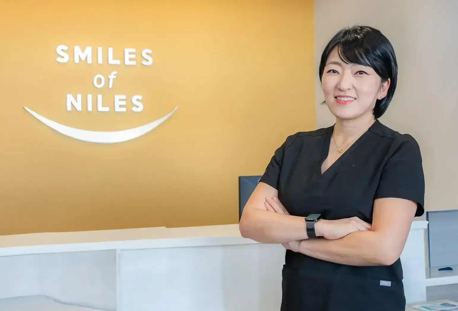 Woman in black scrubs smiling with arms crossed near 